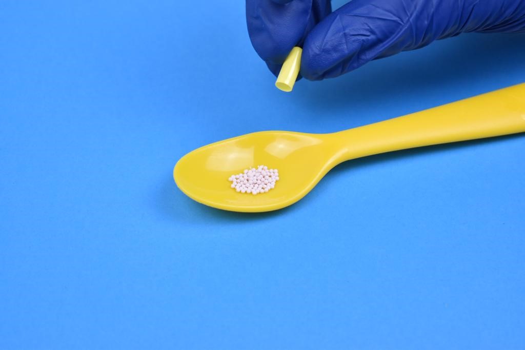Shows the contents of the capsule poured onto a spoon. The contents consists of many small balls of medication